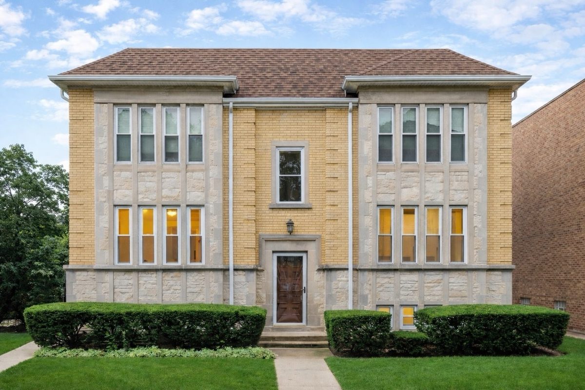 Symmetrical three-story brick and limestone apartment building with trimmed hedges