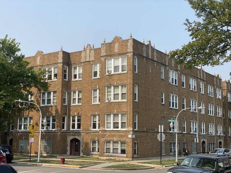 Three-story brick courtyard apartment building on a tree-lined street